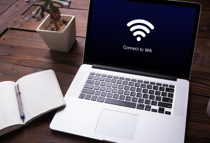 Laptop sitting on a desk with a screen that says "Connecting to WiFi", sitting beside a book and a plant 