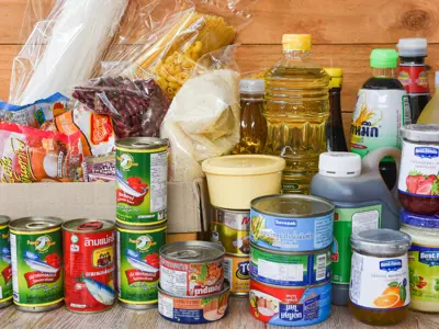 Box of canned goods, rice, pasta and cooking oil on a table.