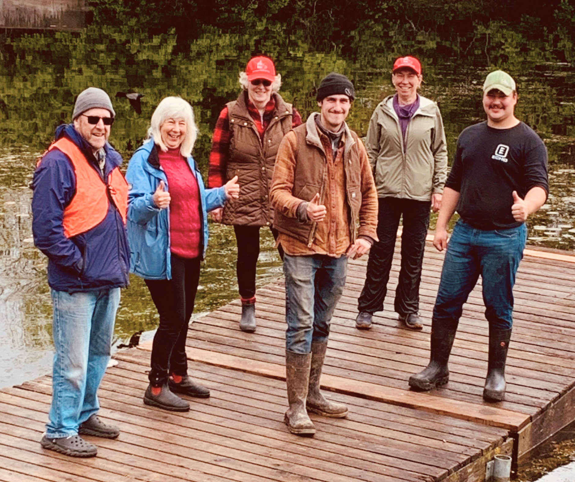 six smiling people standing on a dock in the river