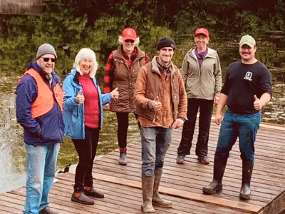 six smiling people standing on a dock in the river