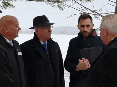 Four people stand together outdoors in light snow having a conversation, with a snowy field in the background.