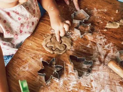 Child pressing cookie cutter into dough on a floured wooden table.