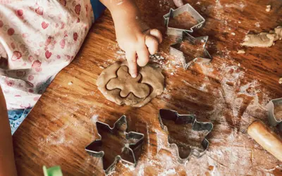 Child pressing cookie cutter into dough on a floured wooden table.