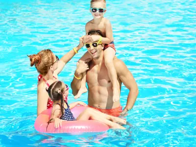 Family playing in a pool with a float and wearing sunglasses.