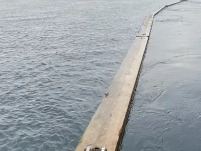 Wooden ice boom sections float on a river with buoys in the distance.