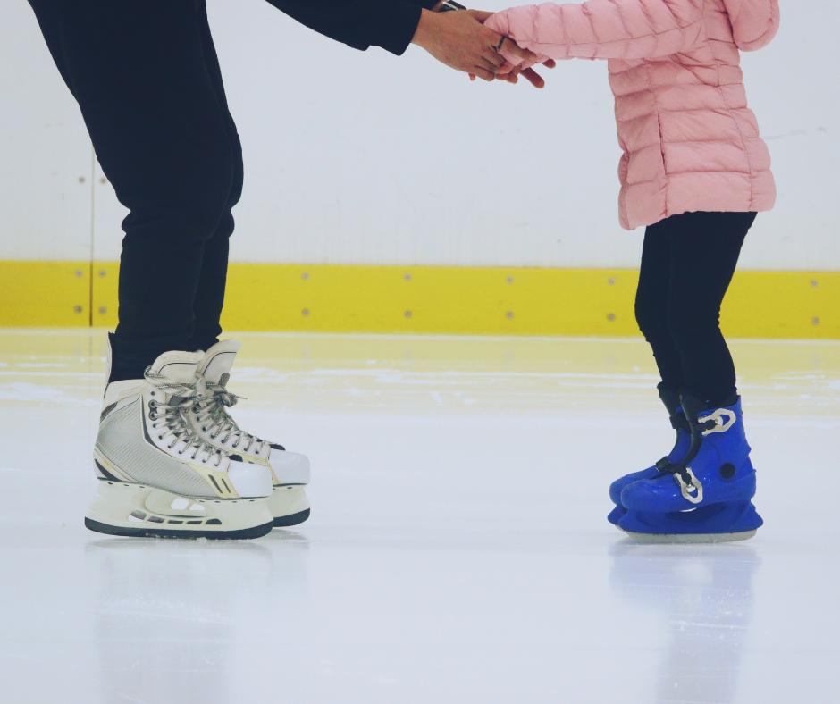 Adult helping a child learn to skate on an indoor ice rink.