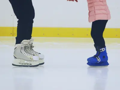 Adult helping a child learn to skate on an indoor ice rink.