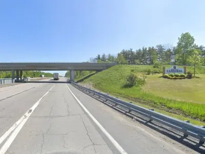 Highway view of an overpass with vehicles travelling in both directions and the Cardinal welcome sign on a grassy slope to the right.