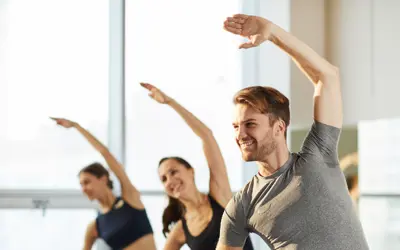 Group of adults in a fitness class stretching with one arm overhead.
