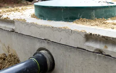 The concrete structure of a septic tank with black inlet pipe and green plastic access lid.