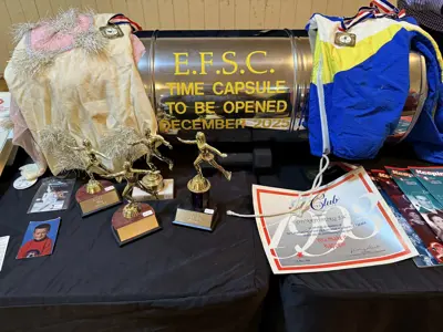 Time capsule with figure skating trophies, papers and clothing on a table.