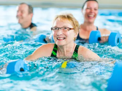 Older adults exercising in a pool with foam water weights.