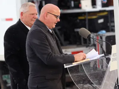 A speaker stands at a podium under a canopy while another person stands behind him.