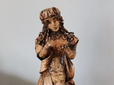 papier-mâché statue of a girl with braids in period clothing, standing on a wooden base.