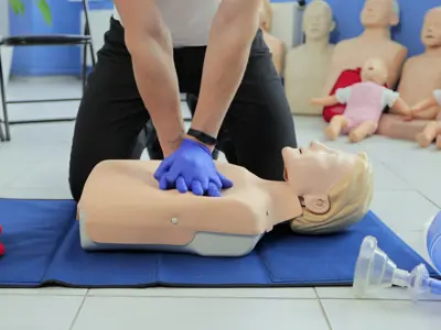 Person wearing gloves performing CPR on a training mannequin in a class.