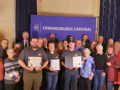 Large group gathered with certificates and an award in front of TWPEC backdrop.