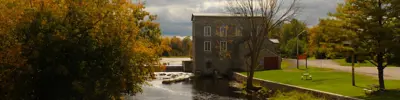 Historic Stone Mill reflected in a river on a fall day with colourful trees.