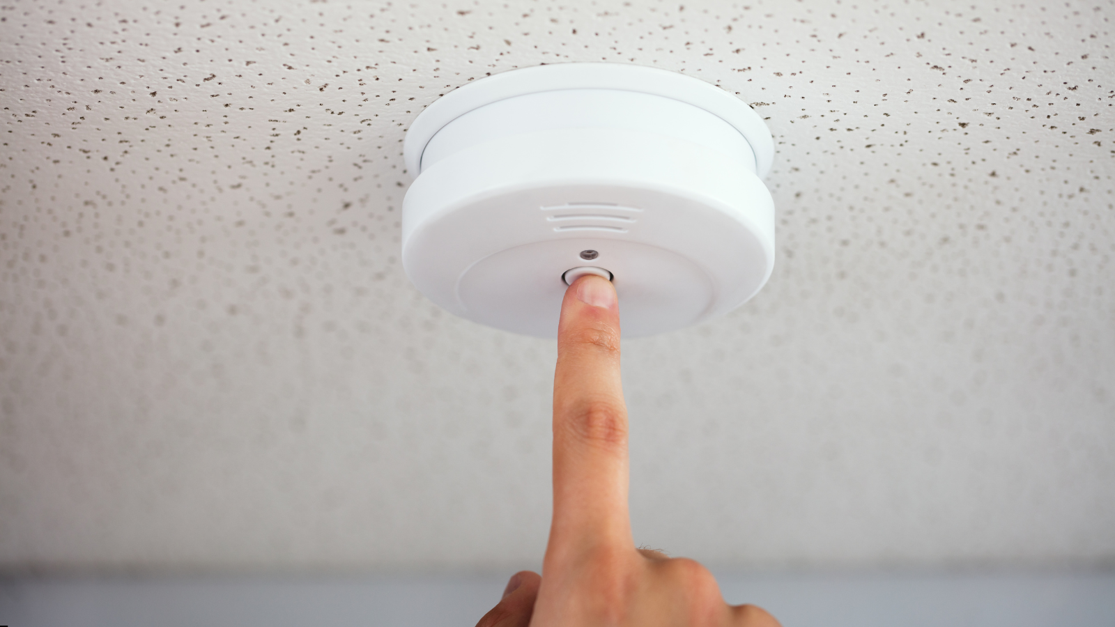 finger pushing button on a smoke detector on ceiling