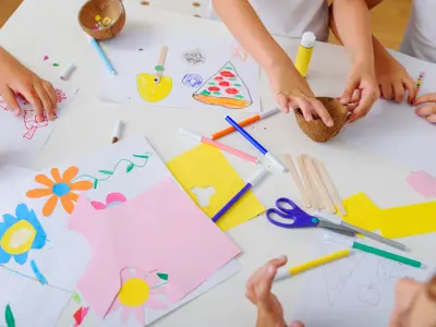 Children’s hands doing crafts with paper, markers, glue, and scissors.