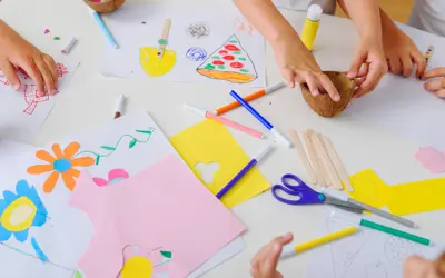 Children’s hands doing crafts with paper, markers, glue, and scissors.