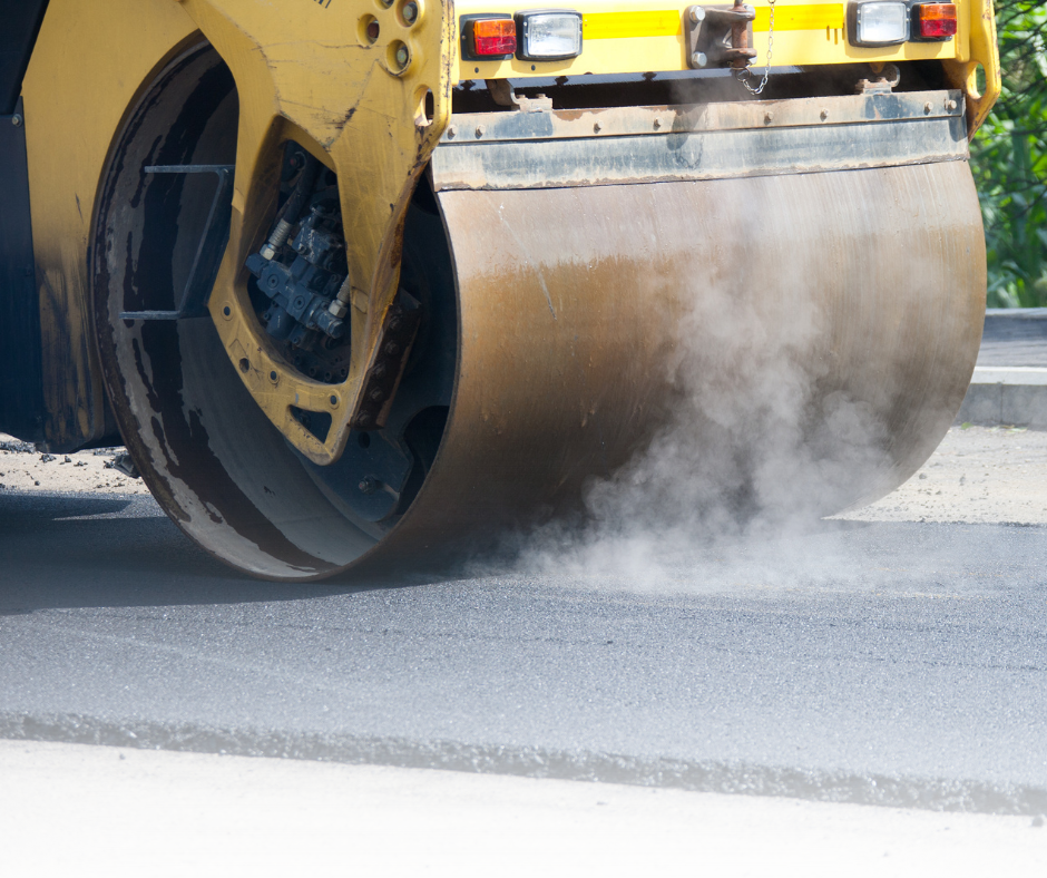 Steamroller compressing fresh asphalt during road or sidewalk paving.