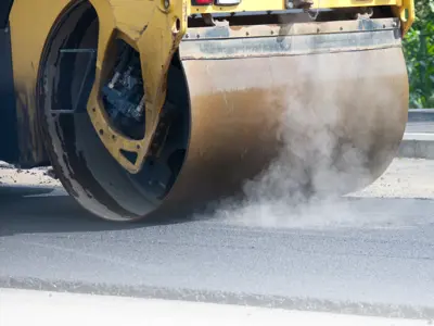 Steamroller compressing fresh asphalt during road or sidewalk paving.
