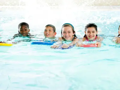 Children holding kickboards and smiling during swim lessons.
