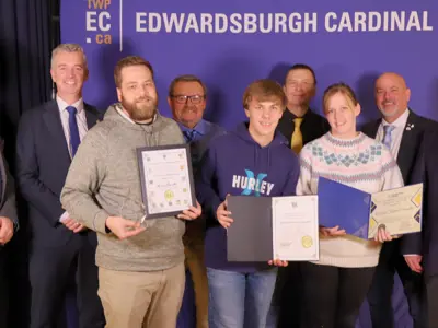 Group of people holding certificates and an award in front of TWPEC backdrop.